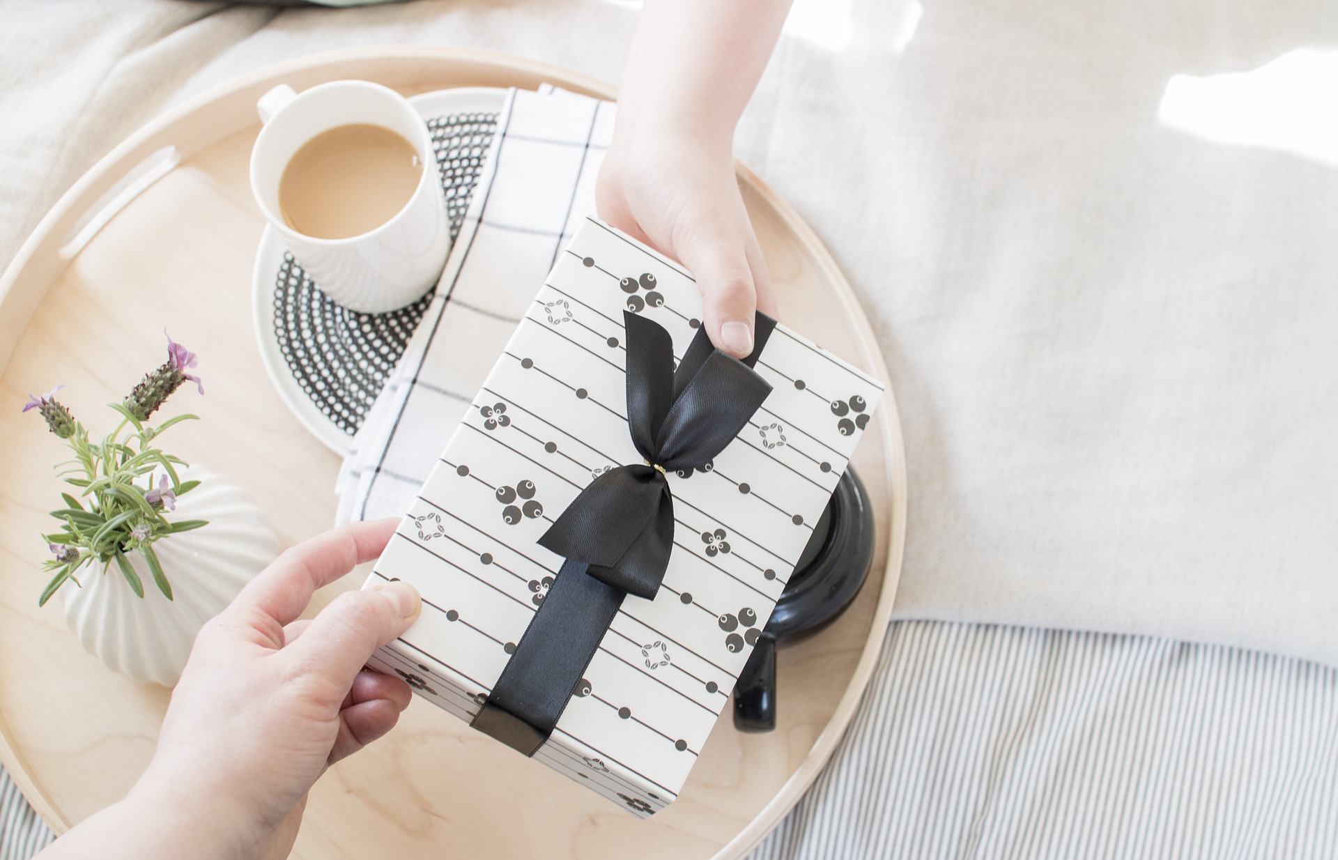 a hand reaching out to take a beautifully wrapped gift with a black ribbon